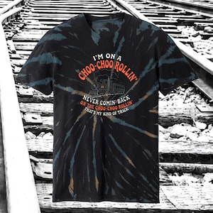 May include: A black short-sleeve t-shirt with a blue and brown tie-dye spiral pattern. The center features a graphic of a steam locomotive with the text: I'M ON A CHOO-CHOO ROLLIN' NEVER COMIN' BACK ON THE CHOO-CHOO ROLLIN' THAT'S MY KIND OF TRACK.