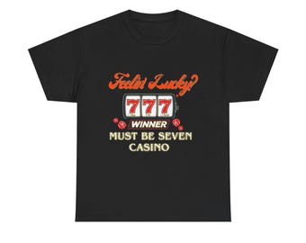 May include: Black t-shirt with a casino-themed graphic. The design features the text "Feelin' Lucky?" in orange, a slot machine with "777" in the windows, and the words "Winner" and "Must Be Seven Casino". Two red dice are also included.