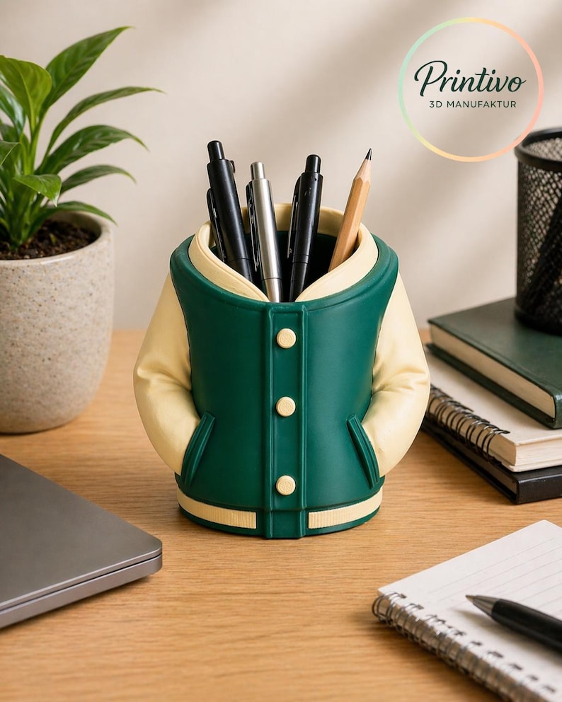 May include: A green and cream-colored desk organizer shaped like a varsity jacket, holding pens and a pencil. The organizer has three buttons and two pockets. The Printivo logo is visible in the background.