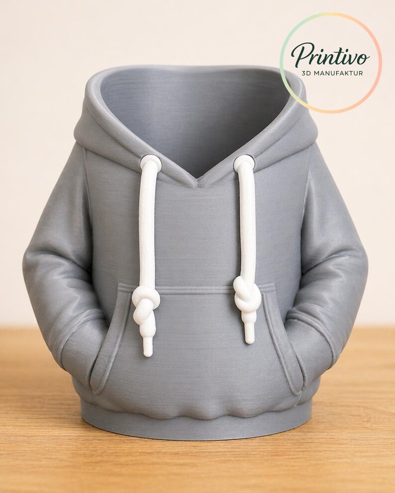 May include: A gray 3D-printed hoodie-shaped container with white drawstrings and a front pocket. The container has a hood and is designed to resemble a miniature sweatshirt. The Printivo logo is visible in the upper right corner.