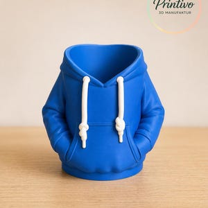 May include: A blue hoodie-shaped decorative container with white drawstrings and a hood. The container has two pockets and is sitting on a wooden surface. The Printivo logo is in the upper right corner.