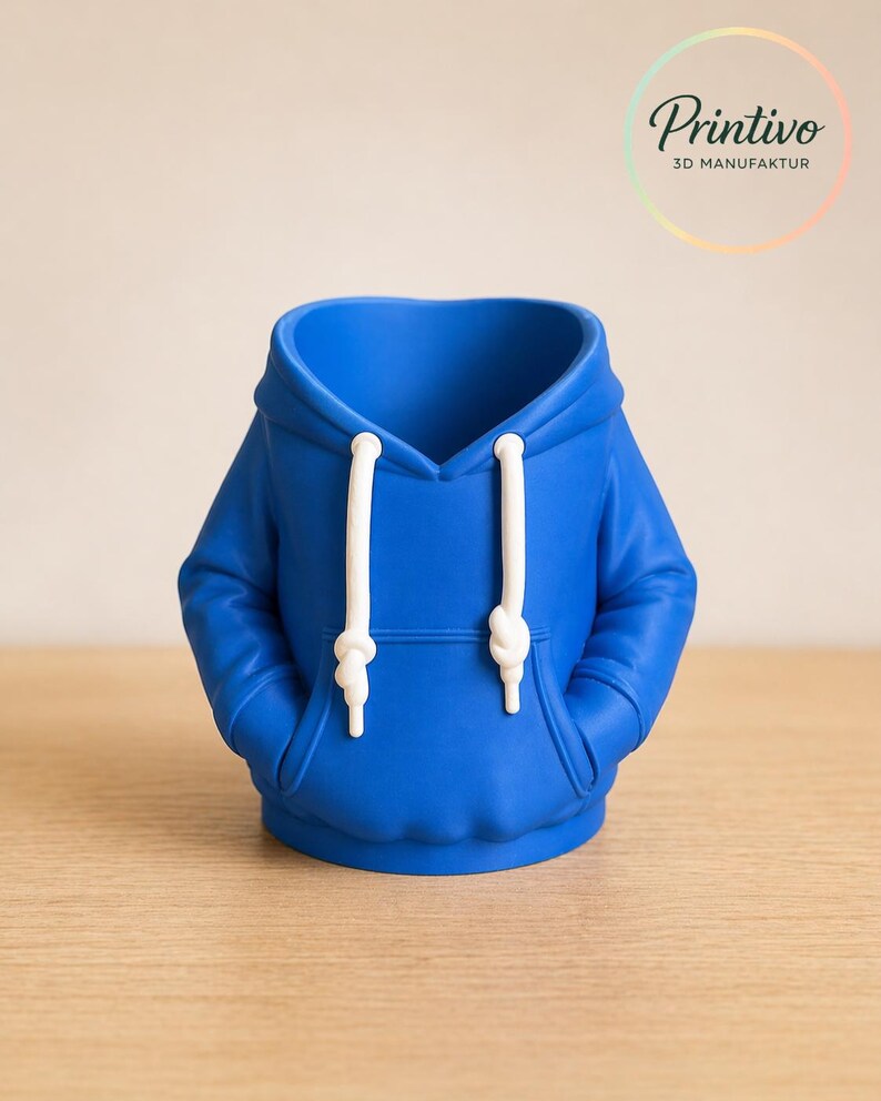 May include: A blue hoodie-shaped decorative container with white drawstrings and a hood. The container has two pockets and is sitting on a wooden surface. The Printivo logo is in the upper right corner.