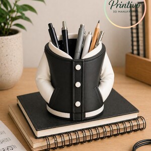 May include: A black and white varsity jacket-shaped pen holder filled with pens and a pencil. The pen holder sits on top of a black notebook and a spiral-bound notebook. The Printivo logo is visible in the background.