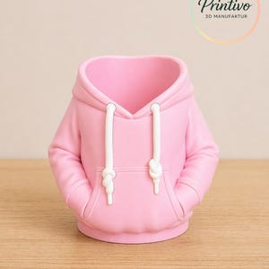 May include: A pink hoodie-shaped container with white drawstrings and pockets. The container is made of a smooth material and sits on a wooden surface. The Printivo logo is visible in the background.