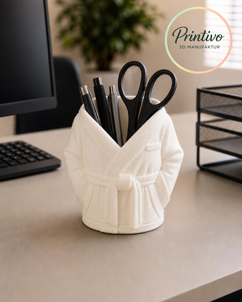 May include: A white robe-shaped desk organizer holding black pens and scissors. The organizer is on a desk with a computer and a plant in the background. The Printivo logo is in the upper right corner.