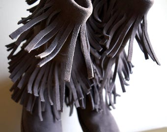 May include: A pair of gray suede boots with fringe detailing. The boots have a pointed toe and a low heel.