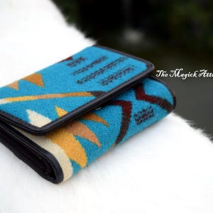 May include: A folded wallet with a turquoise, yellow, and brown geometric pattern. The wallet has a black border and is resting on a white surface. The Magick Attic is written on the top right corner.
