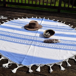 May include: A round, blue and white striped blanket with a white crocheted edge and tassels. A brown hat, a small bowl, and a feather are on the blanket. The Magick Attic is written in the top left corner.