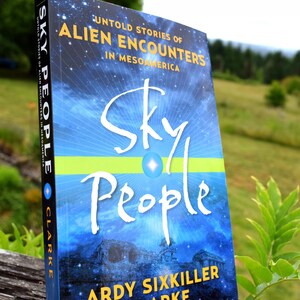 May include: A book titled "Sky People" is displayed on a small stand. The cover features a blue and white design with the title in large, white script. The book's subtitle reads "Untold Stories of Alien Encounters in Mesoamerica."