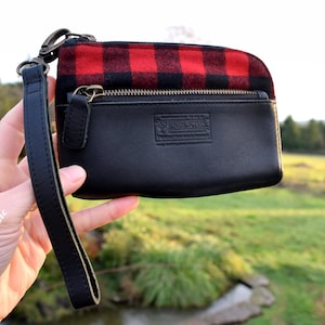 May include: Black leather wristlet with a red and black plaid top. The wristlet has a zipper closure and a black wrist strap. The brand name "Pendleton" is embossed on the front.