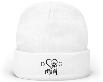 May include: A white beanie with a folded brim. The front of the beanie features a black graphic of a heart, paw print, and the words "DOG MOM". This winter hat is a great gift for dog lovers.