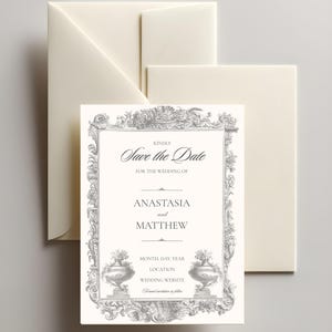 Op de afbeelding: Ivoor trouwkaart met een decoratieve grijze rand en de woorden "Save the Date" bovenaan. De namen "Anastasia en Matthew" staan eronder gecentreerd. Inclusief bijpassende enveloppen.