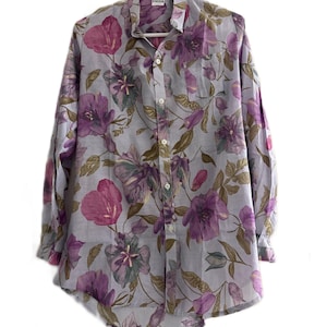 May include: A button-down shirt with a floral pattern. The shirt features a light blue background with large, vibrant purple and pink flowers and green leaves. The shirt has long sleeves and a classic collar. The brand name "KNOOR" is visible at the top.