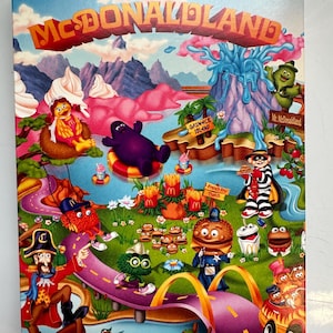 May include: A colorful print featuring the text "WELCOME TO MCDONALDLAND." The image depicts various McDonaldland characters, including Grimace, Mayor McCheese, and the Hamburglar, in a whimsical landscape with a road and water features.