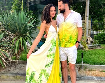 Puede incluir: Una pareja vistiendo ropa a juego con estampado tropical. La mujer lleva un vestido maxi blanco con un diseño de hojas de palma amarillas y verdes. El hombre lleva una camisa blanca con un diseño de hojas de palma amarillas y verdes y pantalones cortos blancos.