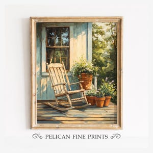 Puede incluir: Una impresión artística enmarcada titulada PELICAN FINE PRINTS que muestra una mecedora de madera en un porche junto a una ventana y tres macetas de terracota con plantas verdes y flores blancas pequeñas, frente a un follaje verde.