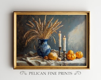 May include: A framed still life painting featuring a blue vase with wheat, lit candles, and pumpkins. The painting has a gold frame and the text "PELICAN FINE PRINTS" at the bottom.