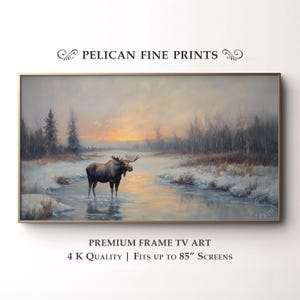 May include: A framed landscape painting featuring a moose standing in a snowy river at sunset. The artwork has a gold frame and includes the text "PELICAN FINE PRINTS" and "PREMIUM FRAME TV ART".