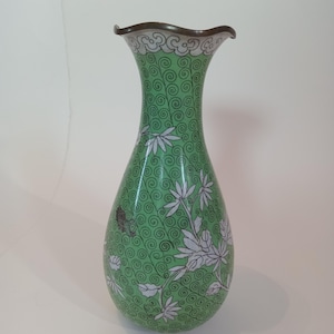 May include: A green decorative vase with a flared rim and a bulbous body. The vase features a swirling pattern and white floral designs. The rim is brown. This vase is a decorative home decor item.