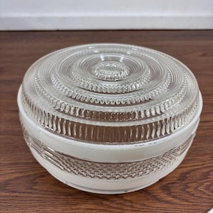 May include: A round glass light fixture shade featuring a clear top section with concentric circular ridges and a textured pattern. The lower portion of the shade is opaque white glass with a horizontal band of embossed crosshatch detailing.