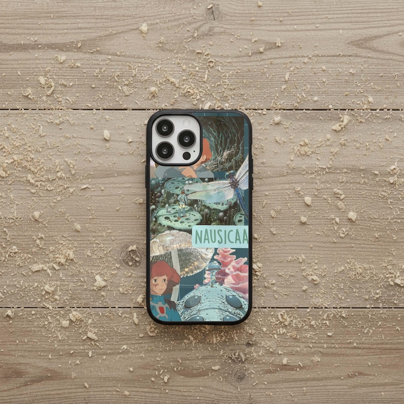 May include: Black phone case featuring a collage of images with a fantasy theme. The design includes illustrations of a girl, mushrooms, and a dragonfly. The word "NAUSICAA" is printed in a light blue font on the case.