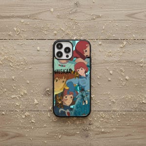May include: Black phone case featuring a collage of anime-style illustrations with a red-haired female character in various poses. The word "NAUSICAA" is printed in white on the case.