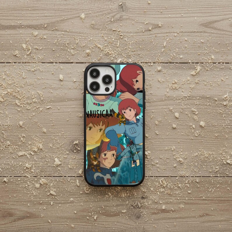 May include: Black phone case featuring a collage of anime-style illustrations with a red-haired female character in various poses. The word "NAUSICAA" is printed in white on the case.