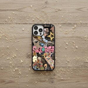 May include: Black phone case with a colorful collage design featuring the text "Soul Eater". The design includes a skateboard, stars, and anime-style illustrations. The case is on a light brown, wood-grain surface.