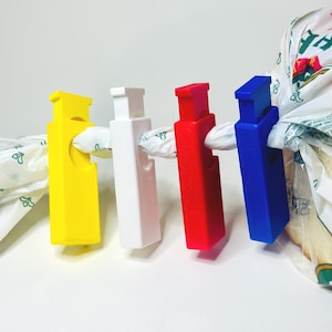 Puede incluir: Cuatro clips de plástico para bolsas en amarillo, blanco, rojo y azul. Cada clip sujeta una bolsa de la compra de plástico cerrada. Los clips son rectangulares con una ranura para sujetar la bolsa.