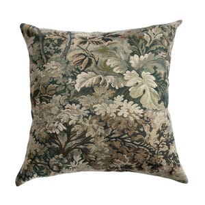 May include: Square decorative pillow with a tapestry-like design featuring a forest scene in shades of green, brown, and cream. The pillow has a textured appearance with detailed depictions of leaves and foliage, creating a natural, rustic aesthetic.