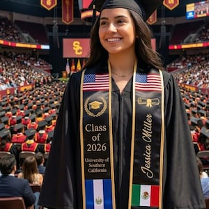 May include: A smiling graduate in a black cap and gown, wearing a sash with the American flag and the text "Class of 2026." The sash also displays the name "Jessica Miller" and flags of other countries. The background shows a crowded graduation ceremony.