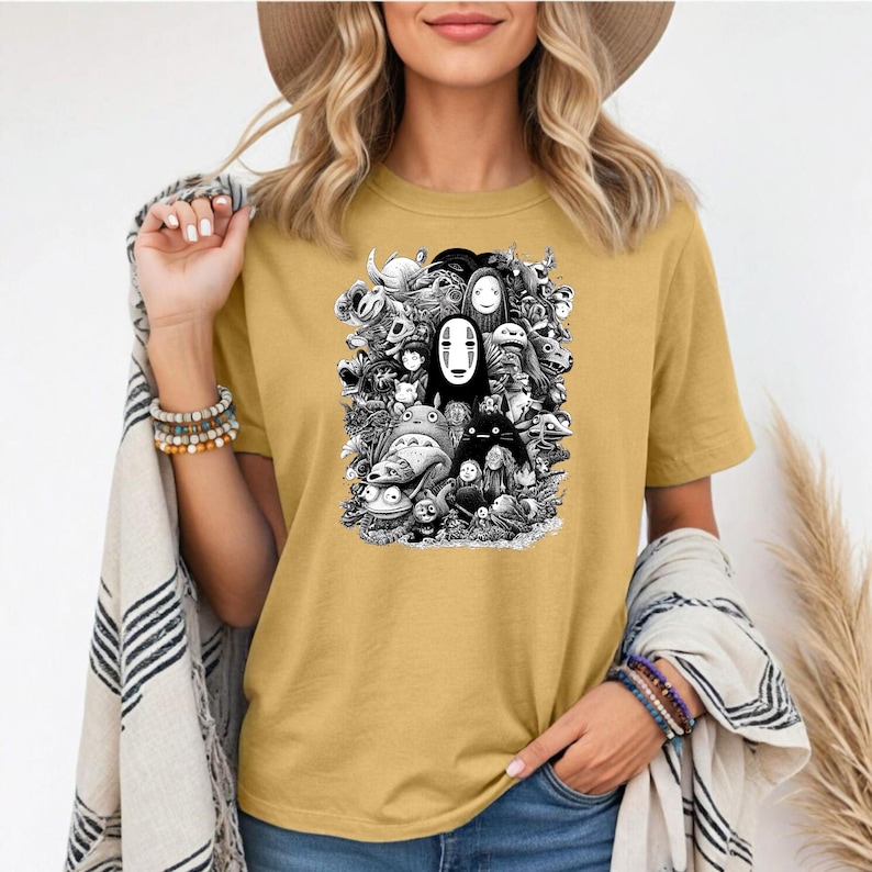 May include: Mustard yellow t-shirt featuring a black and white graphic of characters from a popular animated film. The design includes a variety of creatures and figures, creating a detailed and whimsical composition. The shirt is made of a soft material.