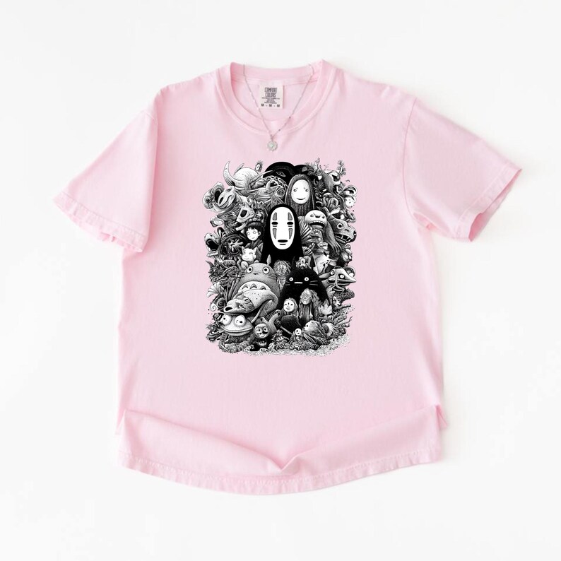 May include: A light pink t-shirt featuring a black and white graphic of various animated characters. The graphic includes characters from a popular animated film. The t-shirt has short sleeves and a crew neck.