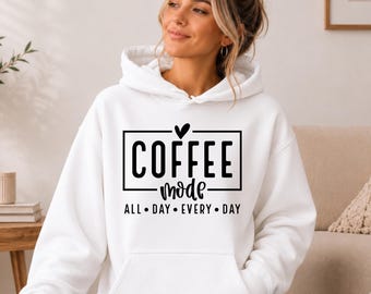 May include: A white hooded sweatshirt featuring black text that reads COFFEE mode ALL DAY EVERY DAY with a small heart icon above the word COFFEE. The garment includes a front kangaroo pocket, long sleeves, and a drawstring hood for a casual look.