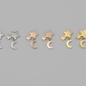 May include: Three pairs of earrings featuring a crescent moon charm with two star charms dangling from it. The earrings are shown in silver, rose gold, and gold.