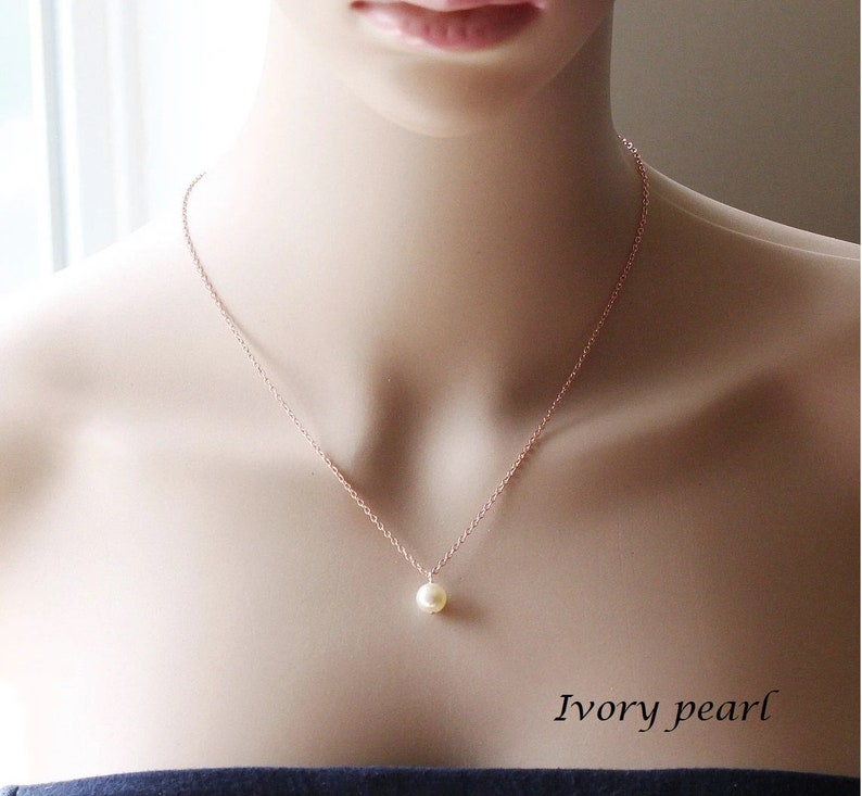 May include: A delicate rose gold chain necklace with a single ivory pearl pendant. The necklace is on a mannequin's neck. The text "Ivory pearl" is below the necklace.
