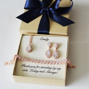 May include: A rose gold jewelry set including a necklace, earrings, and bracelet, presented in a gift box with a navy blue bow. The box contains the text "Emily" and "Thank you for standing by my side, Today and Always!"