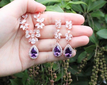 May include: A rose gold jewelry set featuring a necklace and matching drop earrings. Each piece displays a teardrop-shaped dark amethyst stone surrounded by clear crystals, with additional leaf-shaped crystal accents. Text reads # 23 Dark Amethyst.