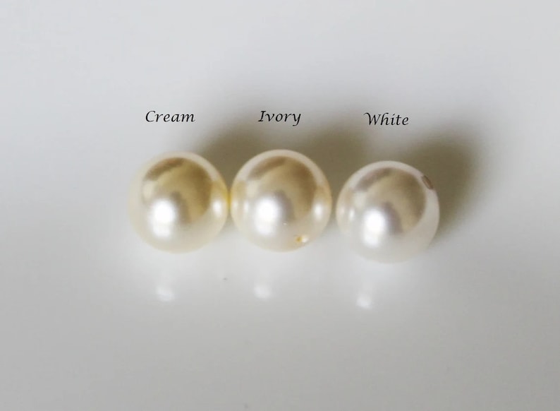 May include: Three round pearls in different shades of white: cream, ivory, and white.