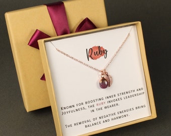 May include: A gold necklace with a small ruby pendant and a leaf charm. The necklace comes in a gold box with a burgundy ribbon. The card reads "Ruby. Known for boosting inner strength and joyfulness, the ruby invokes leadership in the wearer. The removal of negative energies bring balance and harmony."