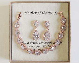 May include: A rose gold jewelry set featuring a bracelet and two drop earrings with pear-shaped clear stones. The set is presented in a box with a card that reads Mother of the Bride and includes a sentimental message about a bride.