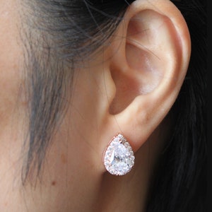 May include: Rose gold stud earrings with a pear-shaped clear crystal surrounded by smaller clear crystals.