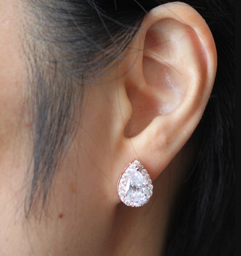 May include: Rose gold stud earrings with a pear-shaped clear crystal surrounded by smaller clear crystals.