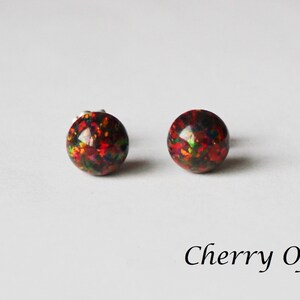 May include: A pair of silver stud earrings with round, red, black, and green opal stones. The earrings are called "Cherry Opal".