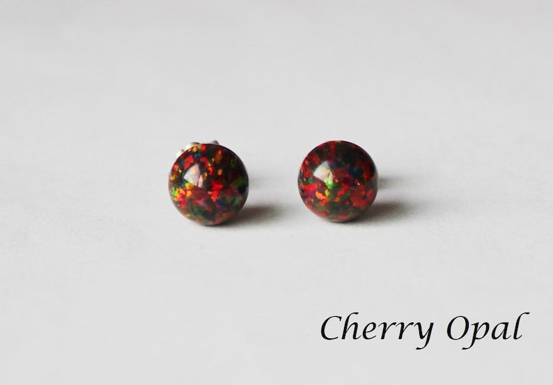 May include: A pair of silver stud earrings with round, red, black, and green opal stones. The earrings are called "Cherry Opal".