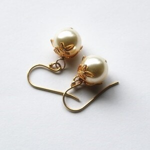 May include: A pair of gold tone earrings with white pearl drops and a floral design on the top of the pearl.