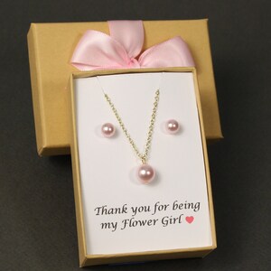 May include: A small gift box with a pink ribbon and a white card inside. The card says "Thank you for being my Flower Girl" with a pink heart. The box contains a pink pearl necklace and earrings.