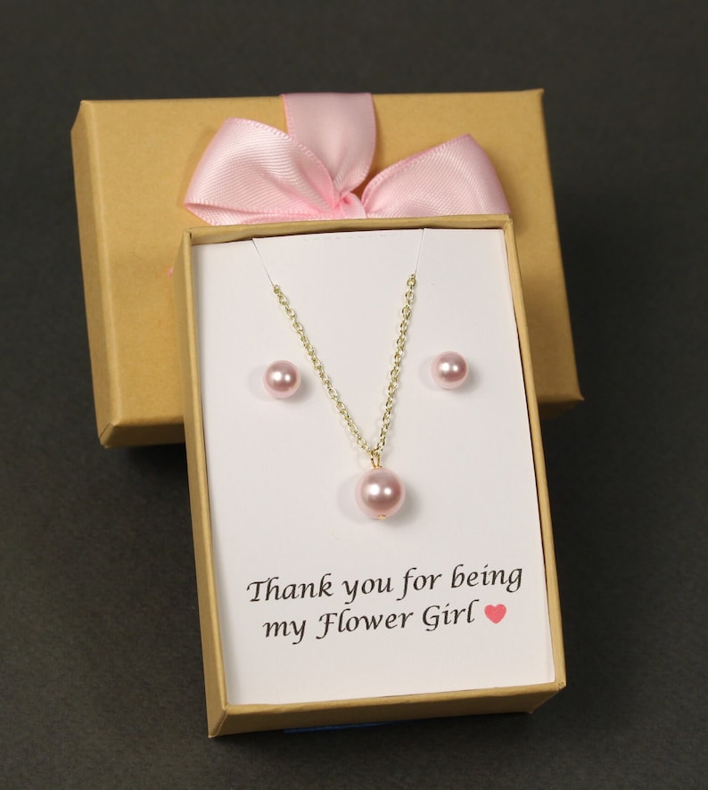 May include: A small gift box with a pink ribbon and a white card inside. The card says "Thank you for being my Flower Girl" with a pink heart. The box contains a pink pearl necklace and earrings.