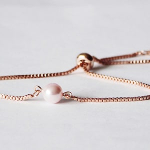 Puede incluir: Un delicado brazalete de cadena de oro rosa con un solo dije de perla. El brazalete es ajustable con un nudo deslizante.