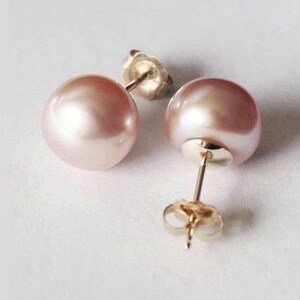 May include: A pair of stud earrings featuring round, light pink pearls with a smooth, lustrous finish. Each pearl is mounted on a gold-toned metal post with a matching gold-toned butterfly clutch backing, showing the hardware clearly.
